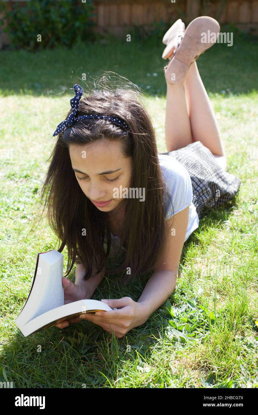 Ein Foto von einem 11-jährigen Mädchen, das in ihrem Garten ein Buch liest Stockfoto