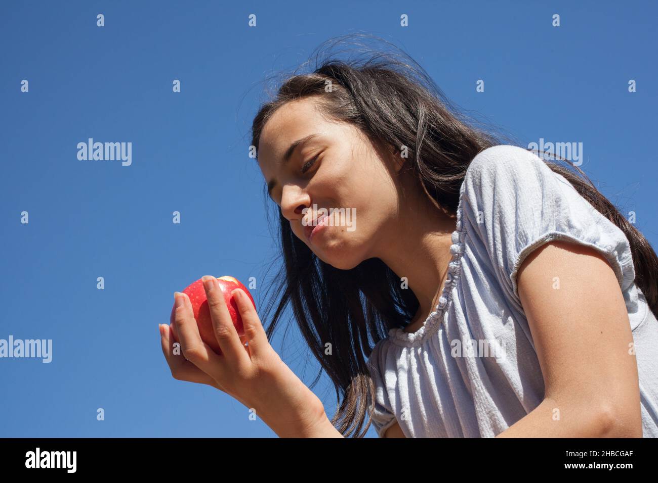 Ein Mädchen, das einen Apfel mit einem tiefblauen Himmel hinter sich isst Stockfoto