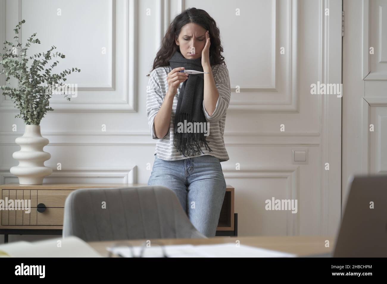 Ungesunde ängstliche Geschäftsfrau im warmen Schal schaut besorgt auf Thermometer Stockfoto