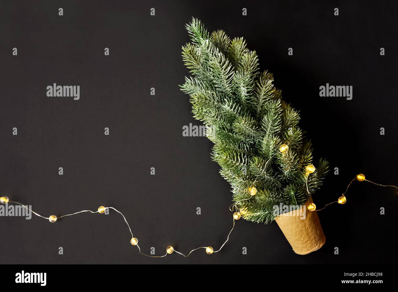 Vorbereitung von Dekorationen für Winterfeste. Künstlicher Weihnachtsbaum, natürlicher Jutefaserstreifen, dunkler Hintergrund, gemütliche Beleuchtung Stockfoto