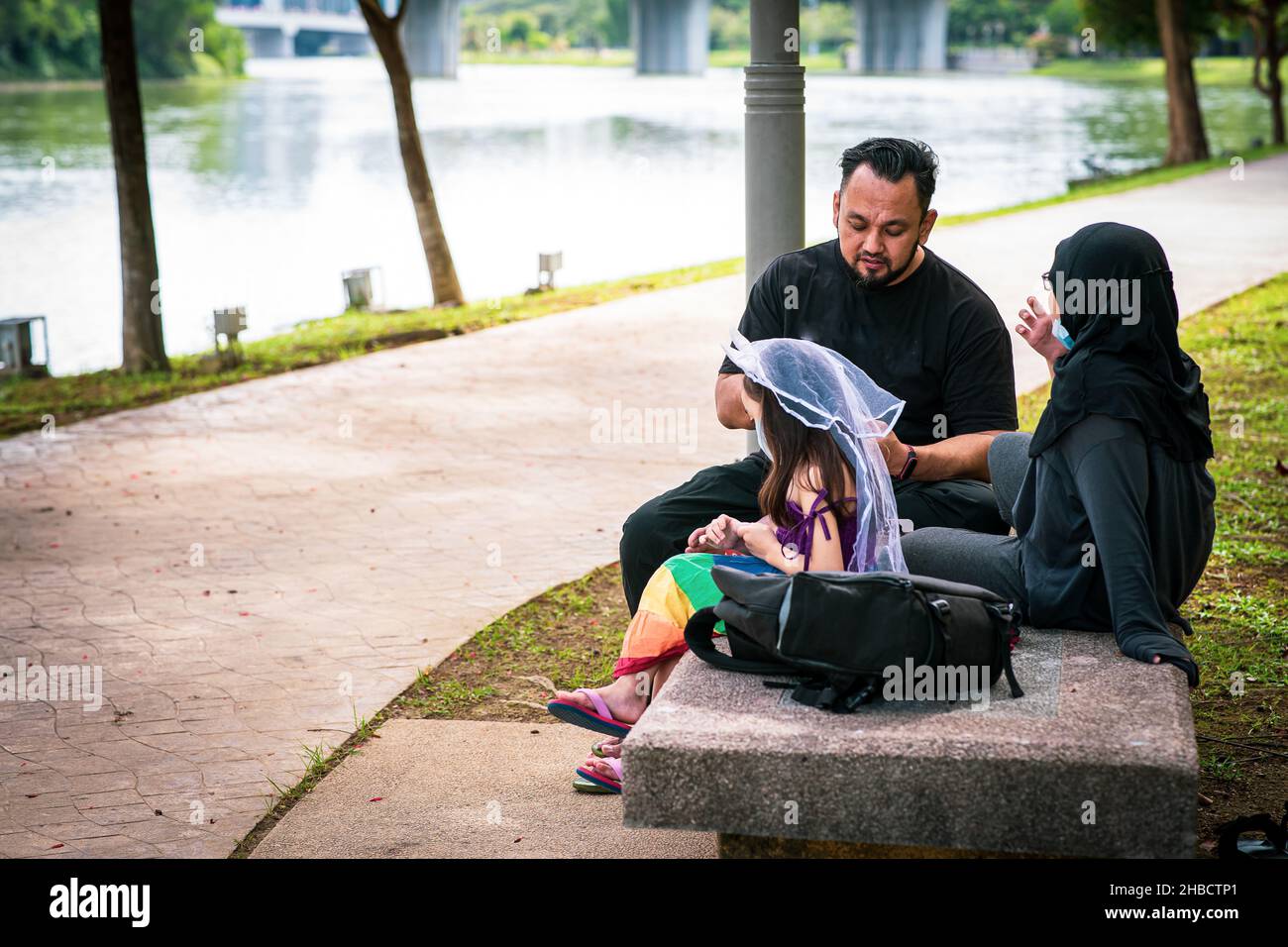 Vater und Kinder sitzen im Park in der Nähe des Sees. Genießen Sie die gemeinsame Zeit. Stockfoto