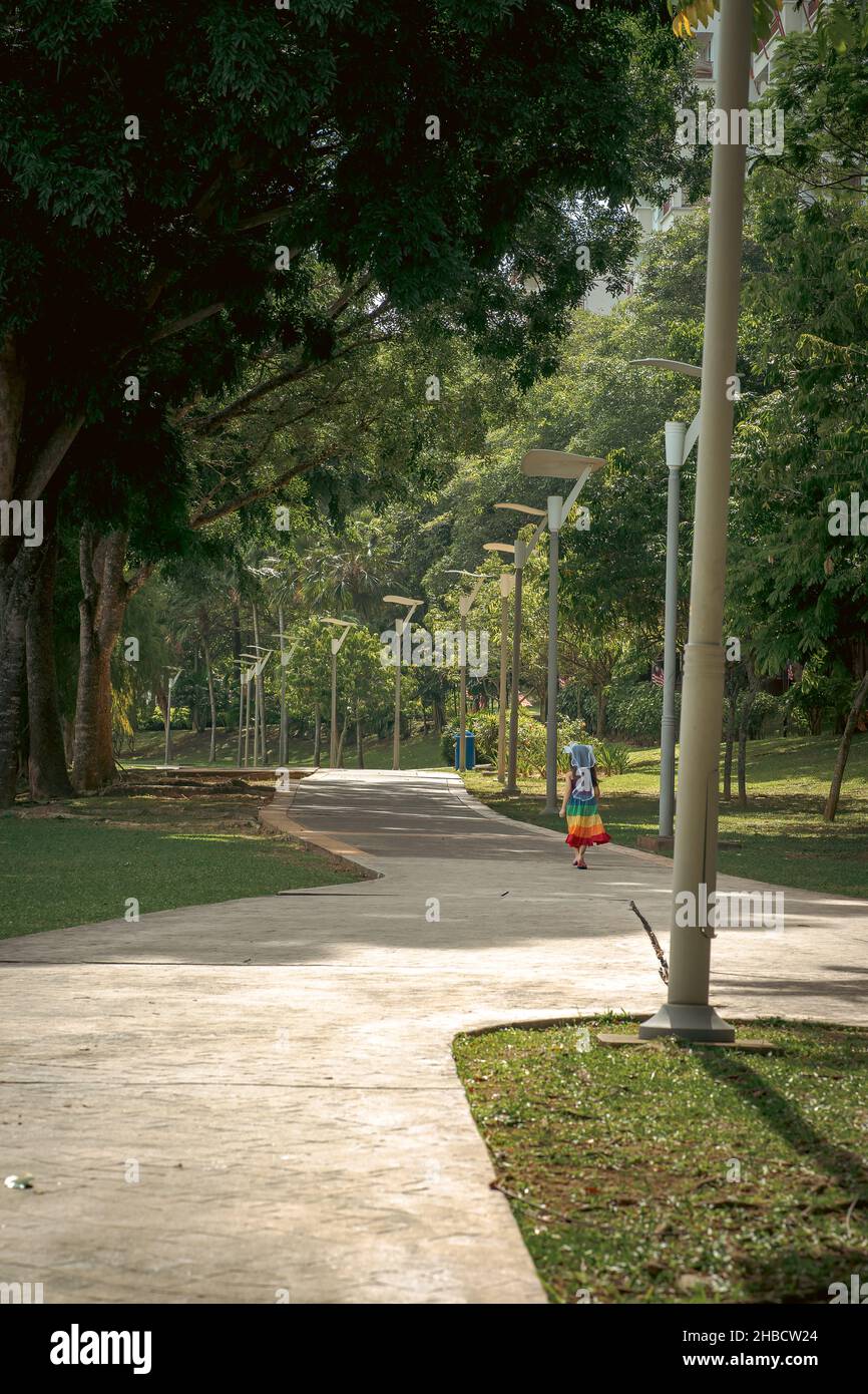 Moderner Park mit Bäumen und Betonweg. Ein Kind, das geht, von hinten gesehen. Stockfoto