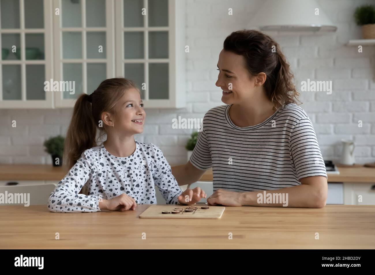 Lächelnd fürsorgliche Mutter und 9s Tochter spielen Holzbrett Spiel Stockfoto