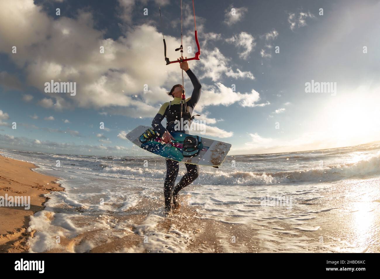 Kitesurfer in schwarzem Neoprenanzug steht am Meeresstrand mit Wakeboard im Wasser und hält Kite Stockfoto