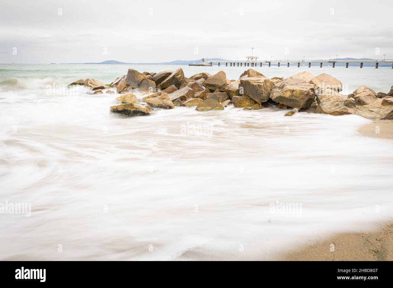 Felsen am Strand mit seidigem Meerwasser und Burgas-Brücke im Hintergrund. Bildende Kunst Bild Bulgarien. Reiseziel 2020. Stockfoto