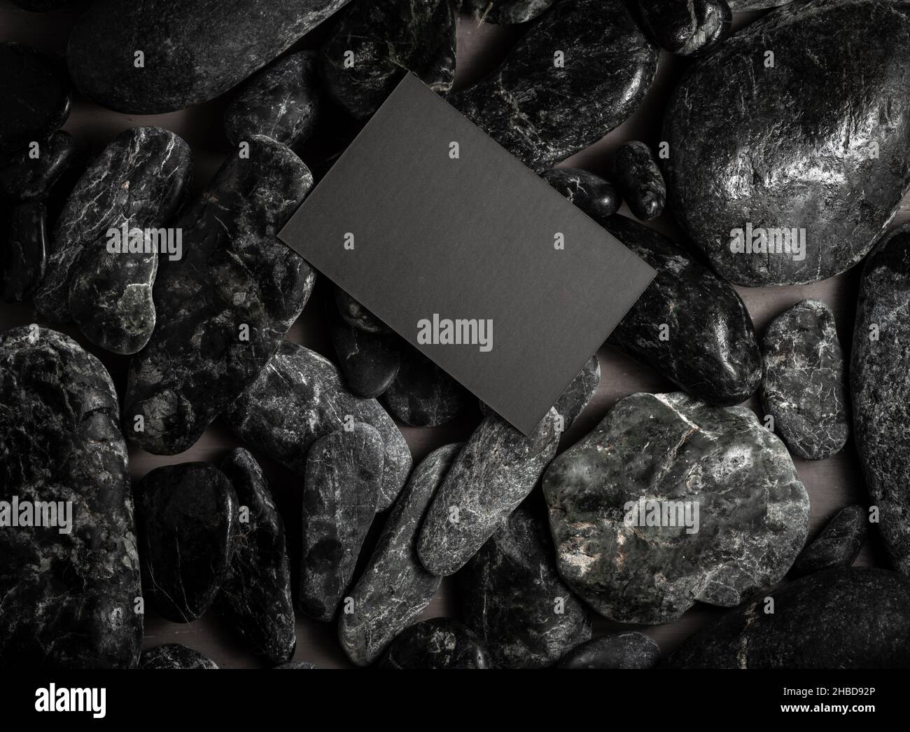 Schwarze imitierte Visitenkarte auf schwarzen Steinen oder Galet, Konzept des Zen Spa oder Sauna Brandings. Stockfoto
