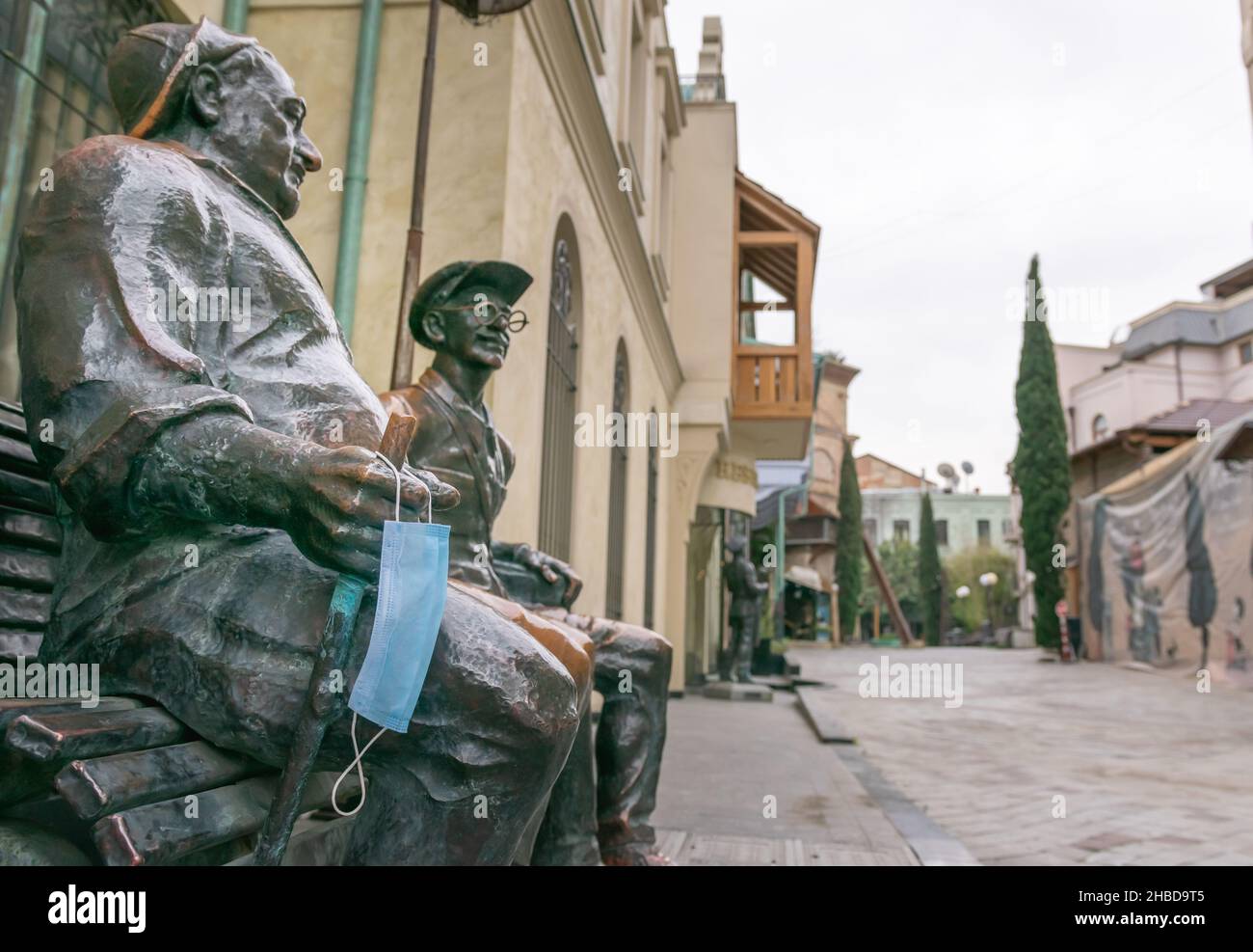 Sitying Gentlemen Statue in Tiflis mit hängender verlorener medizinischer Gesichtsmaske und leerer Straße. Sakartvelo.Georgia.25.03.2020 Stockfoto