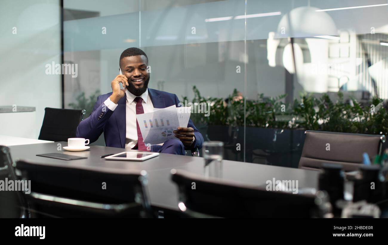 Wohlhabender schwarzer Unternehmer mit Telefongespräch im Büro, Dokumente lesen Stockfoto