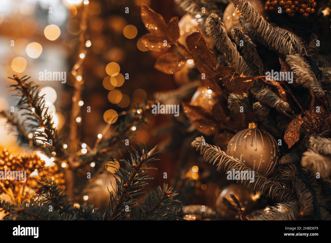 Goldene Weihnachtskugel und glänzende Girlande hängen auf dem Weihnachtsbaum. Winterurlaub Märchen Zusammensetzung und magische Details. Stockfoto