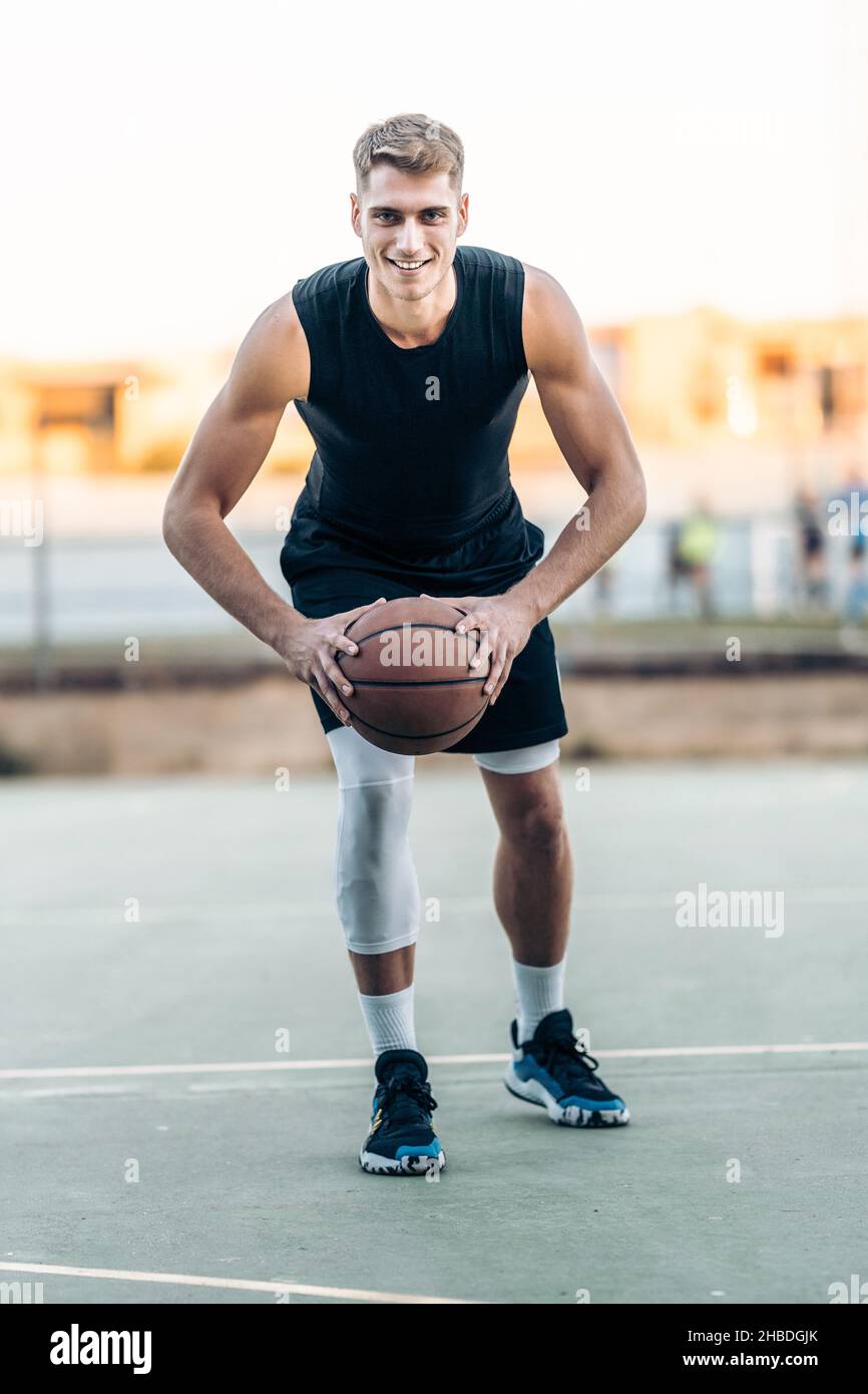 Männlicher Spieler posiert, während er einen Basketball im Freien hält Stockfoto