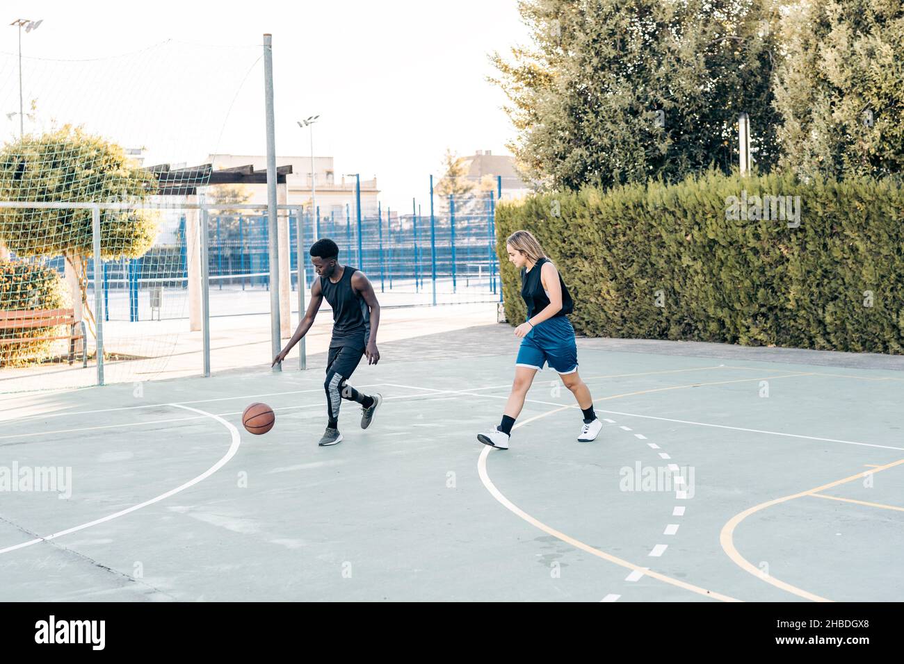 Afrikanischer Mann und blonde Frau spielen Basketball im Freien Stockfoto