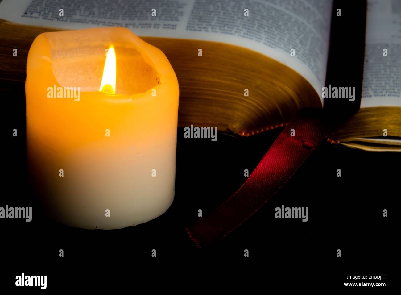 Alte Bibel mit goldenen Seiten, die von Kerzenlicht einer Kerze in der Nähe beleuchtet werden Stockfoto