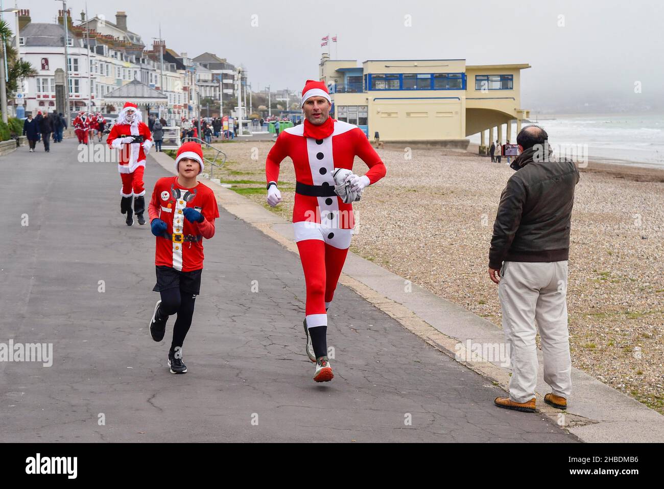 Weymouth, Dorset, Großbritannien. 19th. Dezember 2021. Hunderte von Läufern, die als Weihnachtsmann verkleidet sind, nehmen am jährlichen „The Chase the Pudding“-Vorweihnachtslauf am Strand von Weymouth in Dorset Teil. Die jährliche Veranstaltung wird Geld für die Wohltätigkeitsorganisation will Mackaness Trust sammeln. Frau Pudding läuft auf der Esplanade zum Ziel. Bildnachweis: Graham Hunt/Alamy Live News Stockfoto