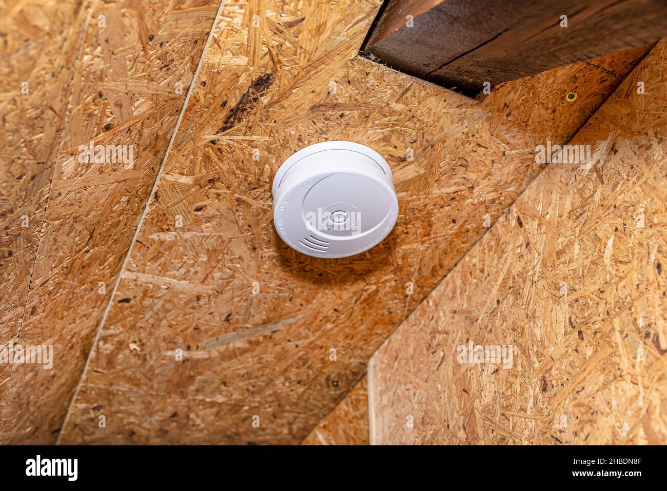 Rauch- und Kohlenmonoxidmelder mit zentraler LED, montiert an einer Decke, die mit OSB-Platinen ausgekleidet ist. Stockfoto