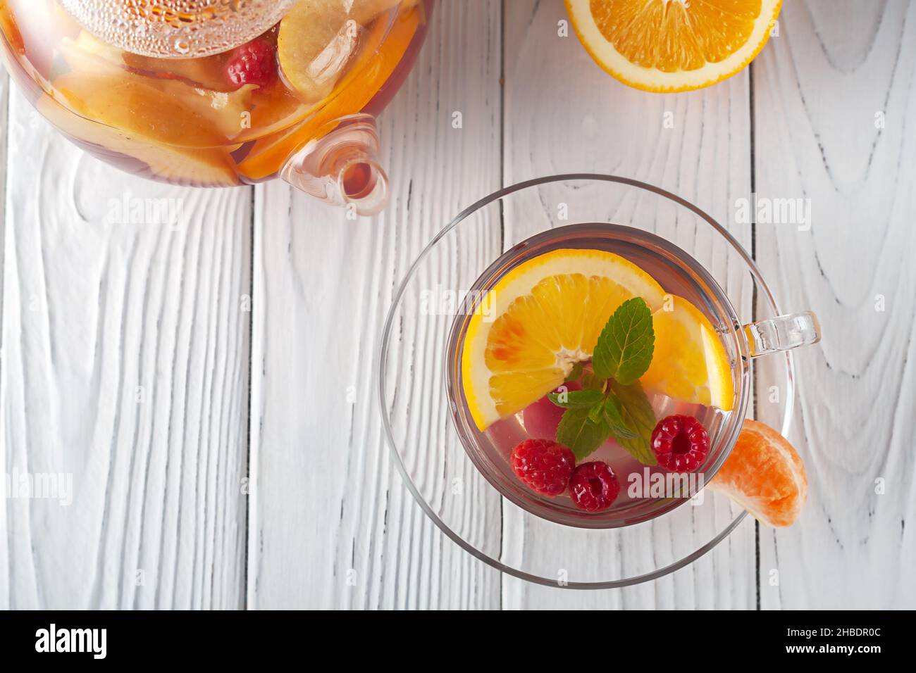 Früchtetee mit Beeren, Orangen und Minze in einer Glasschale auf weißem Holzhintergrund Stockfoto
