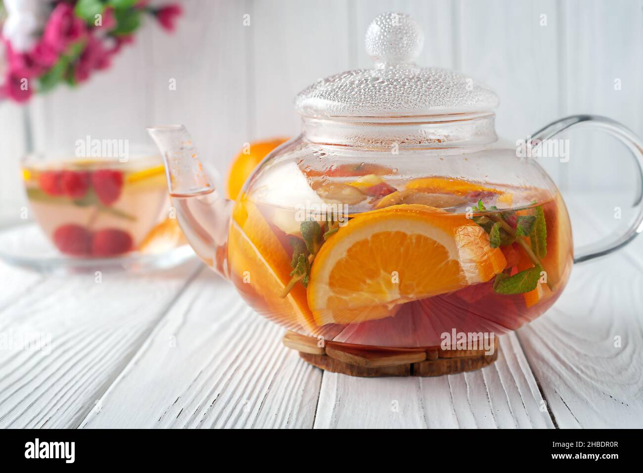 Früchtetee mit Beeren, Orangen und Minze in einer Glas-Teekane auf weißem Holzhintergrund Stockfoto