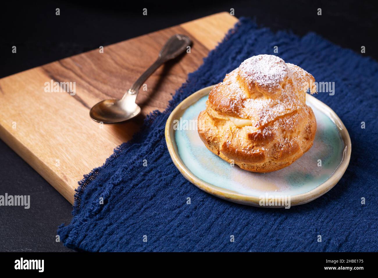 Lebensmittelkonzept hausgemachte frisch gebackene Choux a la Creme, Cream Puff, Choux Cream in weißer Keramikplatte auf schwarzem Hintergrund mit Kopierfläche Stockfoto