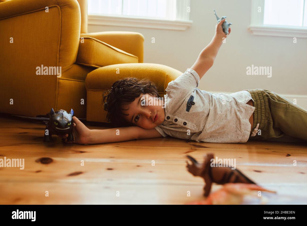 Netter kleiner Junge, der zu Hause mit seinem Spielzeug spielt. Ethnischer Junge, der mit Dinosaurierspielzeug spielt, während er auf dem Boden in seinem Spielbereich liegt. Stockfoto