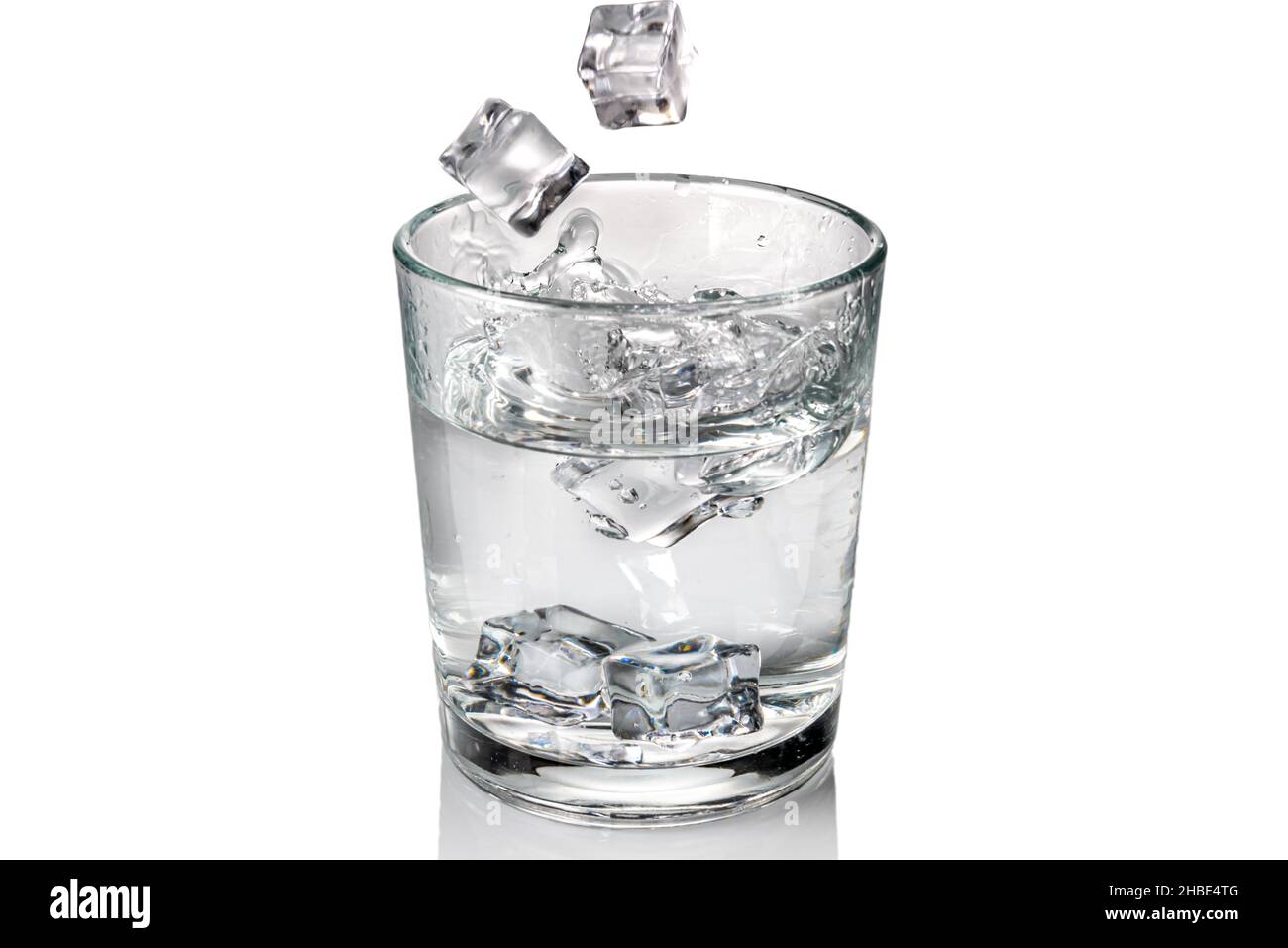 Eiswürfel fallen mit Spritzer in ein Glas mit Süßwasser, isoliert auf Weiß Stockfoto