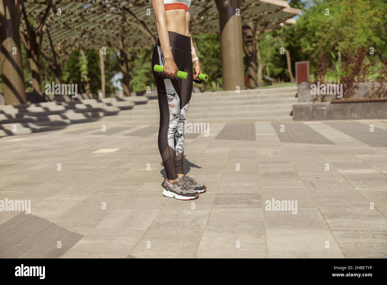 Eine sportliche Dame in stilvollen Leggings hält am Sommertag in der Nähe des Stadtparks Hanteln Stockfoto