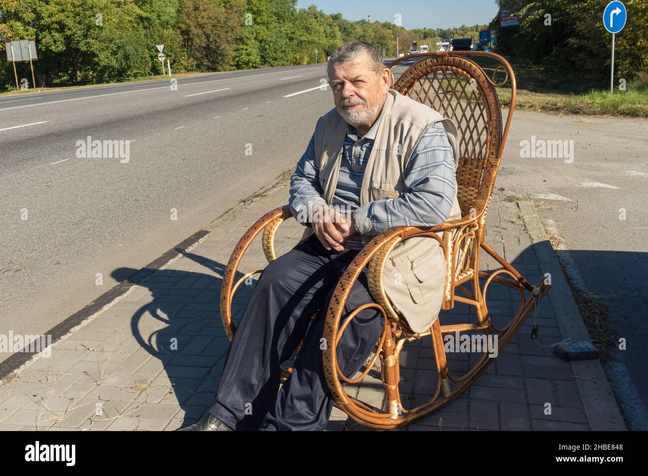 Kaukasischer älterer Mann, der sich ausruhte, während er an einem sonnigen Herbsttag in einem Wicker-Schaukelstuhl am Straßenrand saß Stockfoto