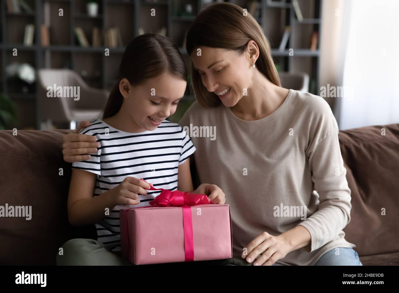 Happy girl sitzen auf dem Sofa mit Mama Auspacken Geschenk-Box Stockfoto