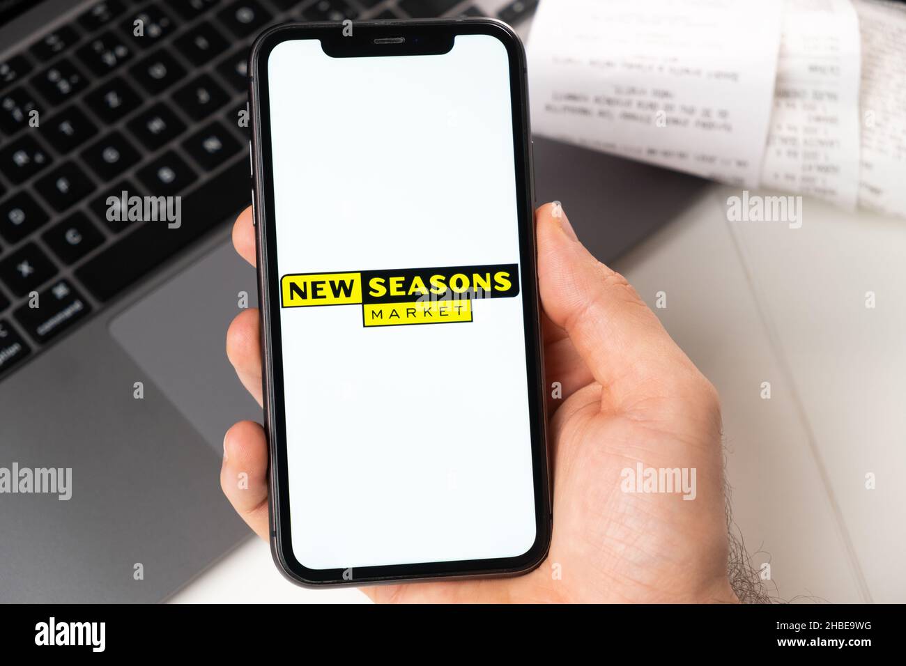 New Seasons Marktanwendung von Supermarkt und Lebensmittelgeschäft in einem Smartphone. Ein Mann hält ein Smartphone mit App zum Einkaufen und einen Laptop im Hintergrund. November 2021, San Francisco, USA Stockfoto