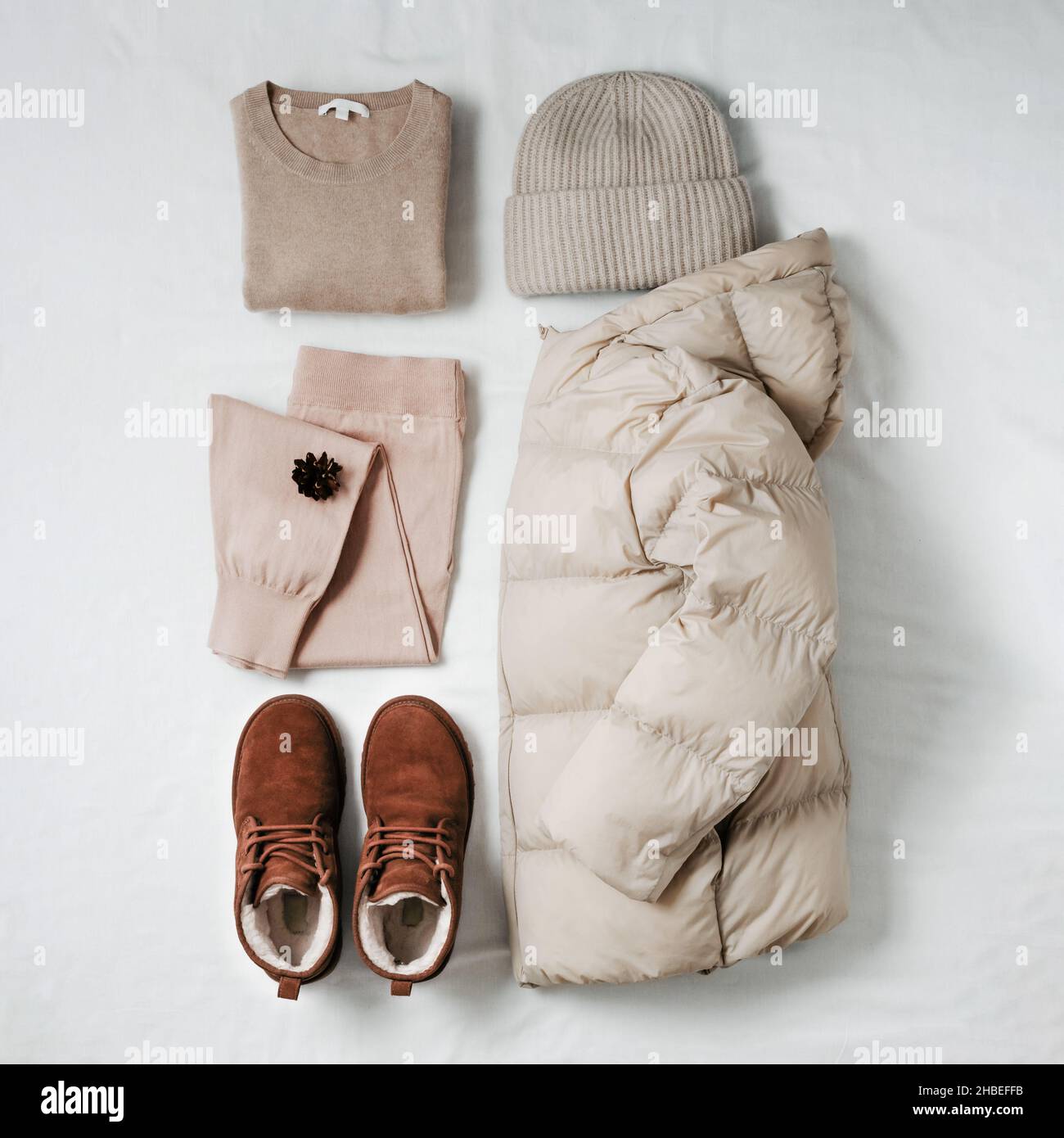 Damen warme leichte Daunenjacke, beiger Kaschmir-Pullover, rosa gestrickte  Jogginghose, gestrickter Bini-Hut, braune Chukka-Wildlederstiefel aus Fell  auf weißem Bettlaken. Kuschelige Winterbekleidung in beige einfarbig  Stockfotografie - Alamy