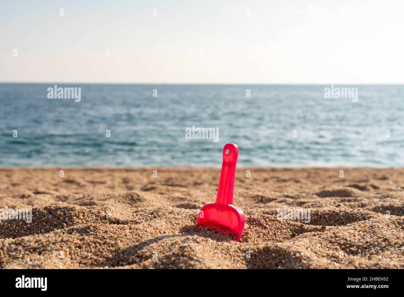 Rote Schaufel im Strandsand mit Meer oder Meer im Hintergrund Stockfoto