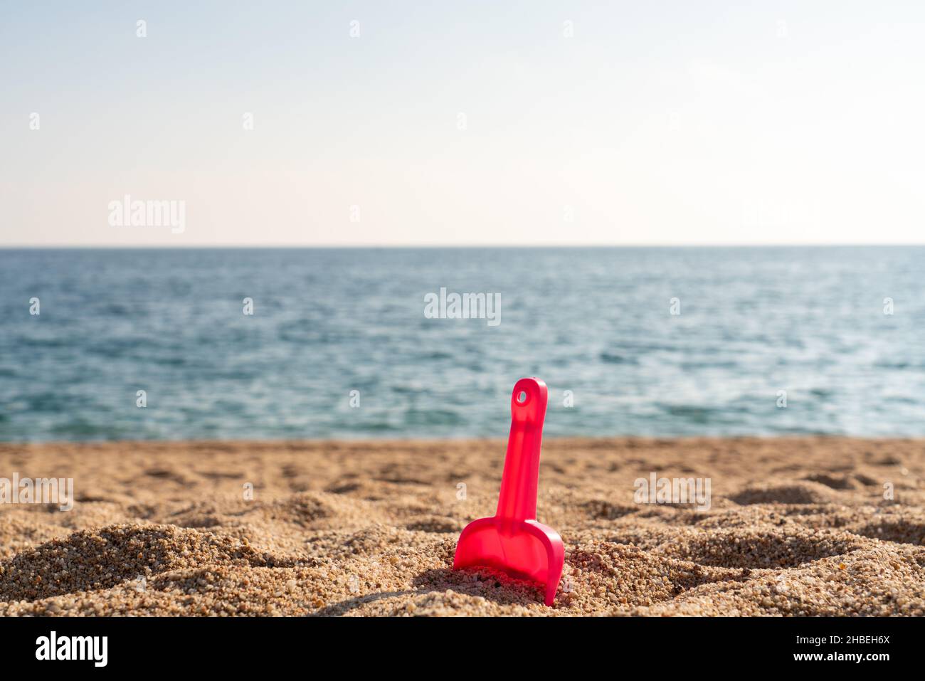 Rote Schaufel im Strandsand mit Meer oder Meer im Hintergrund Stockfoto