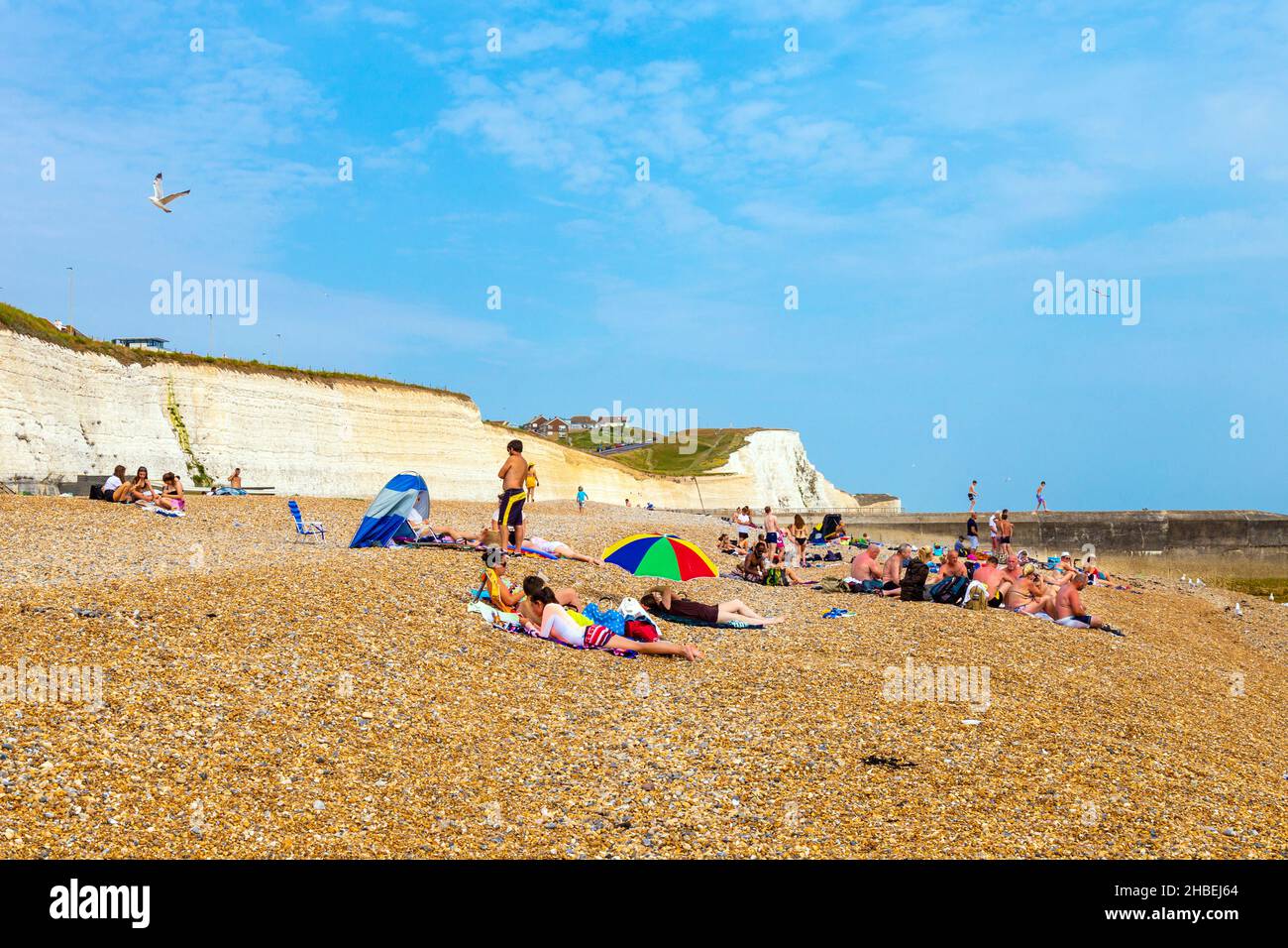 Menschen, die sich an einem Kiesstrand in Saltdean, East Sussex, Großbritannien, entspannen und sonnen Stockfoto