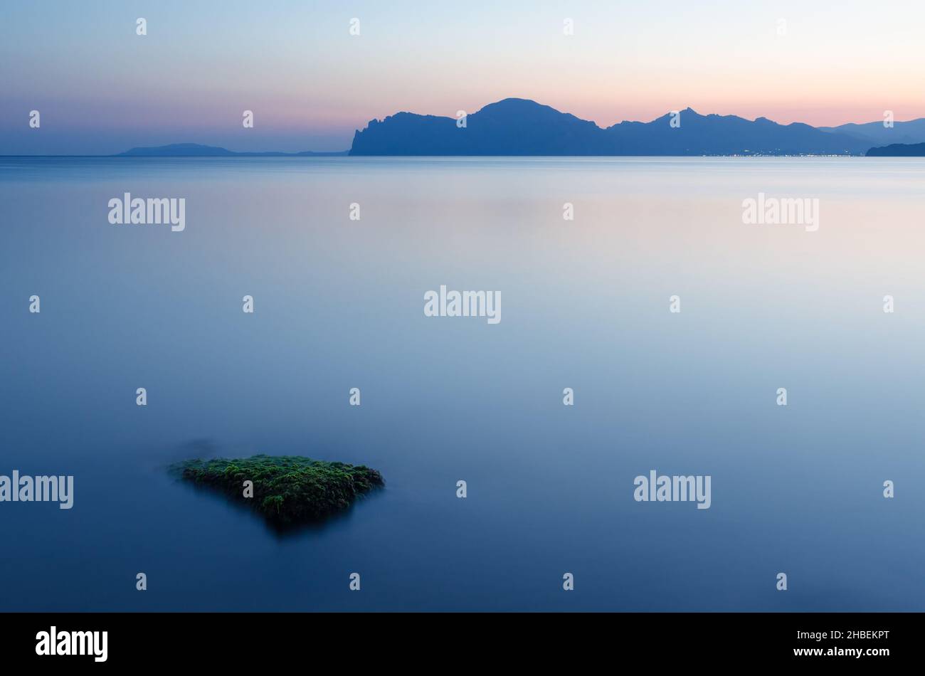 Seascape in der Morgendämmerung. Gebirgskette über dem Horizont. Verschwommenes Wasser bei langer Exposition Stockfoto