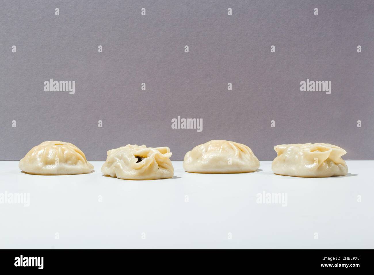 Manty mit Fleisch, Tomaten, Kräutern, Sauce und Pfeffererbsen auf grau minimalistisch Stockfoto