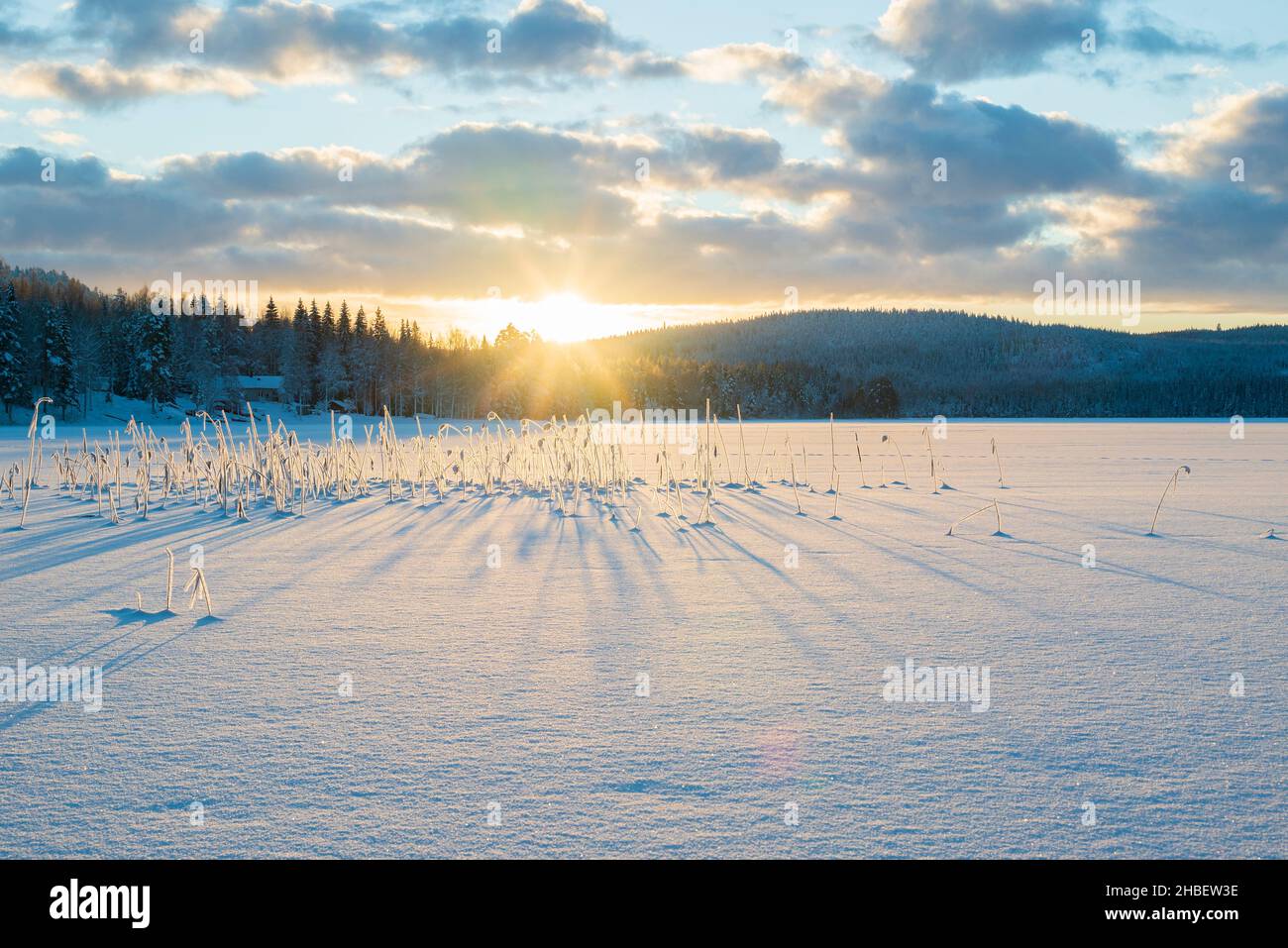 Schneebedeckter See und eine niedrig stehende Sonne am wolkigen Himmel schaffen Schatten im Schnee, Bild aus vasternorrland schweden. Stockfoto