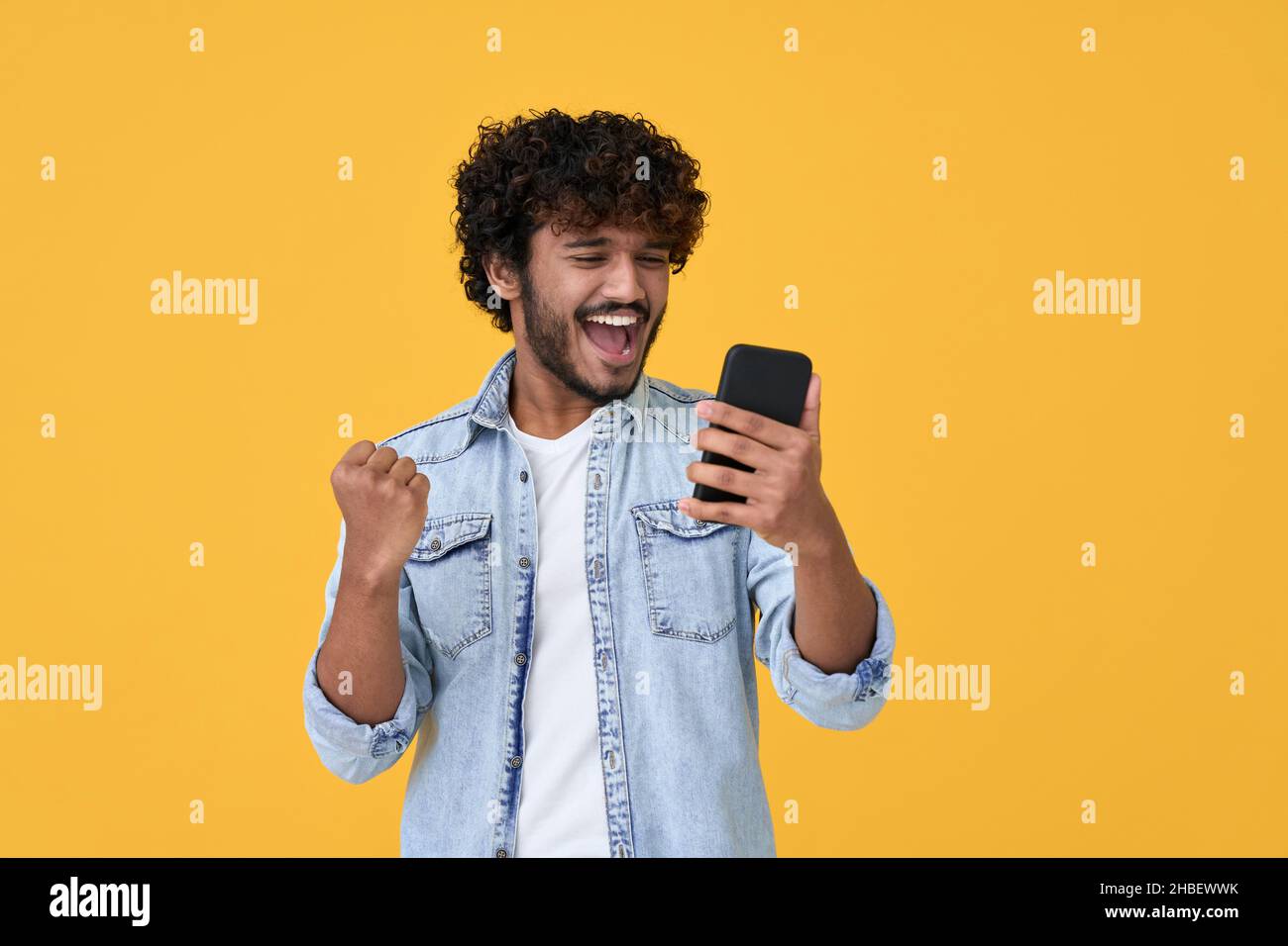 Aufgeregt jungen indischen Mann Gewinner mit Smartphone isoliert auf gelbem Hintergrund. Stockfoto