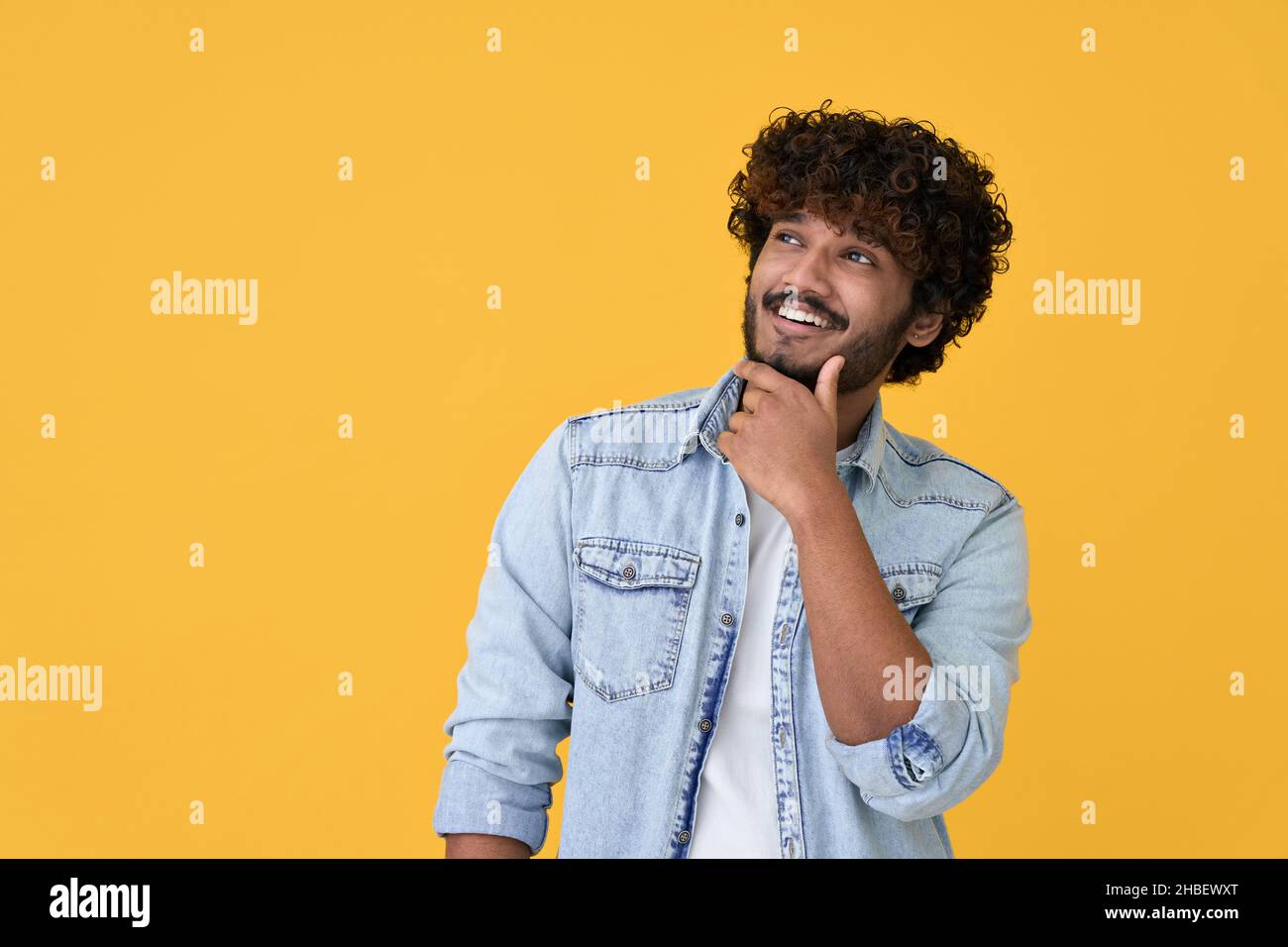Neugieriger junger inder, der auf gelbem Hintergrund schaut, denkt und plant. Stockfoto