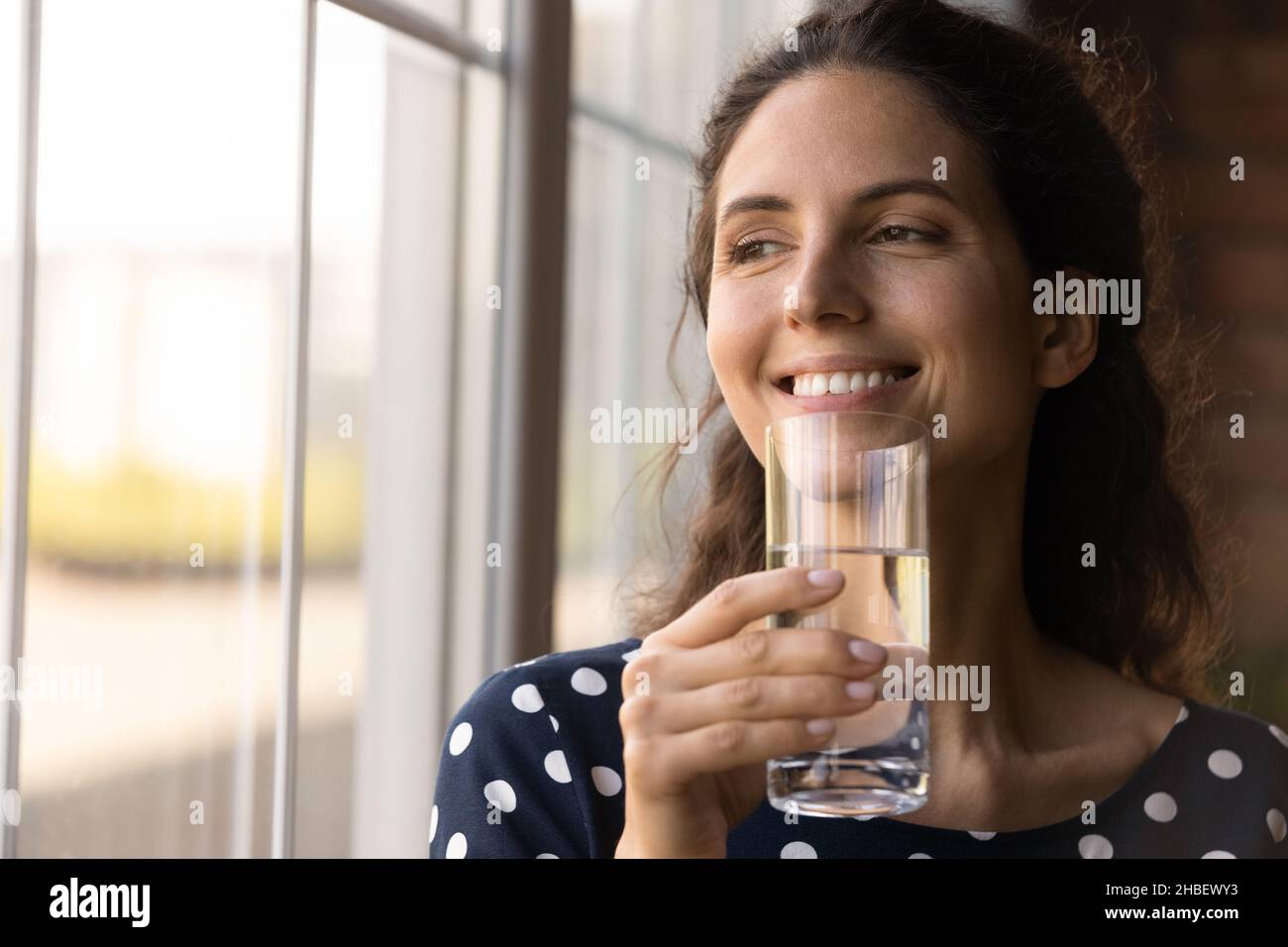 Verträumte friedliche junge hispanische Frau, die ein Glas Wasser trinkt. Stockfoto