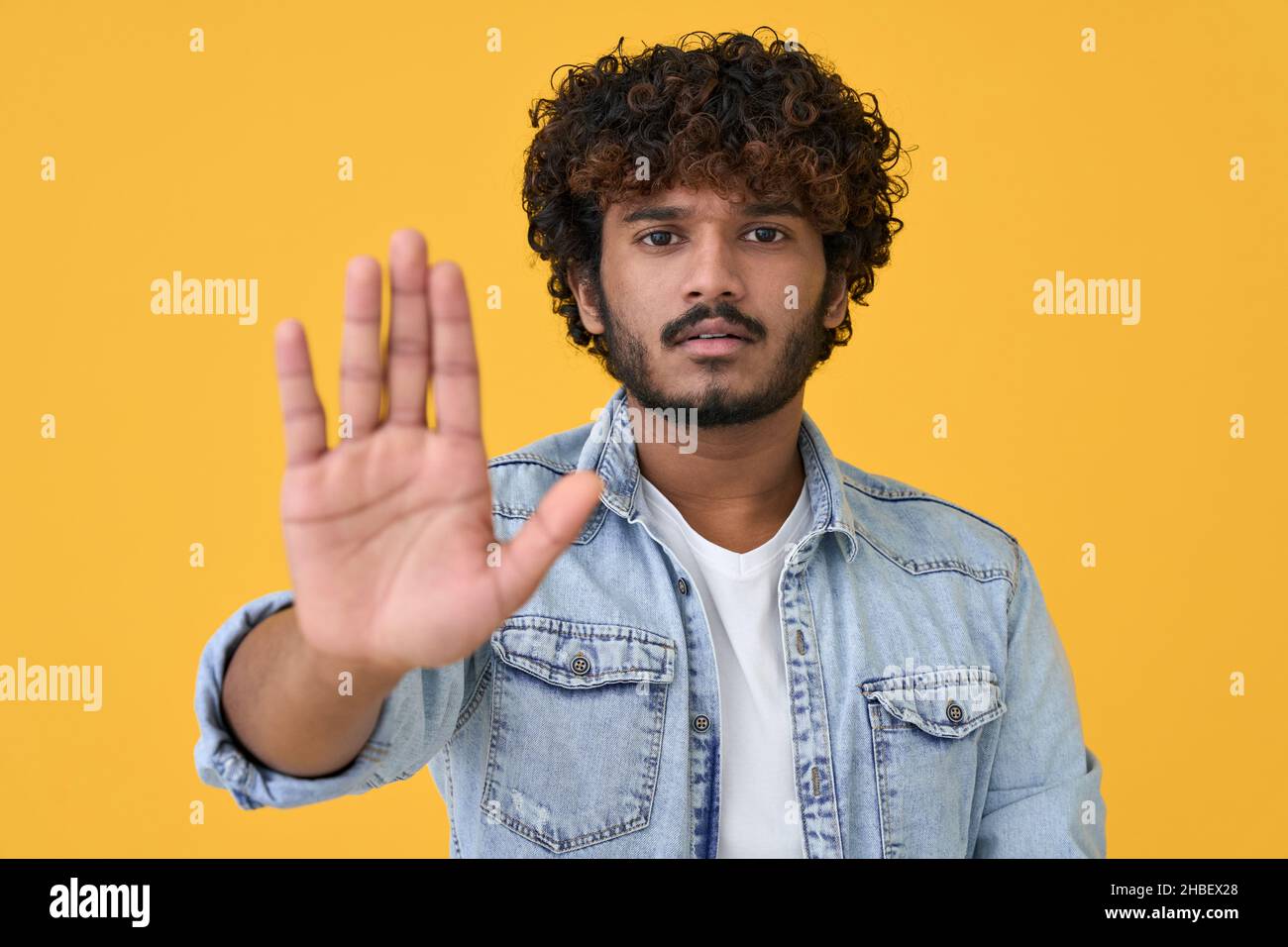 Junger indischer Mann, der auf gelbem Hintergrund eine Stop-Hand-Geste zeigt. Stockfoto