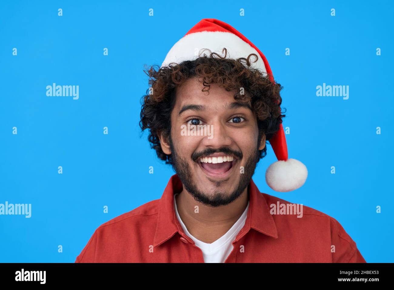 Aufgeregt junger indischer Mann trägt santa Hut isoliert auf blauem Hintergrund. Stockfoto