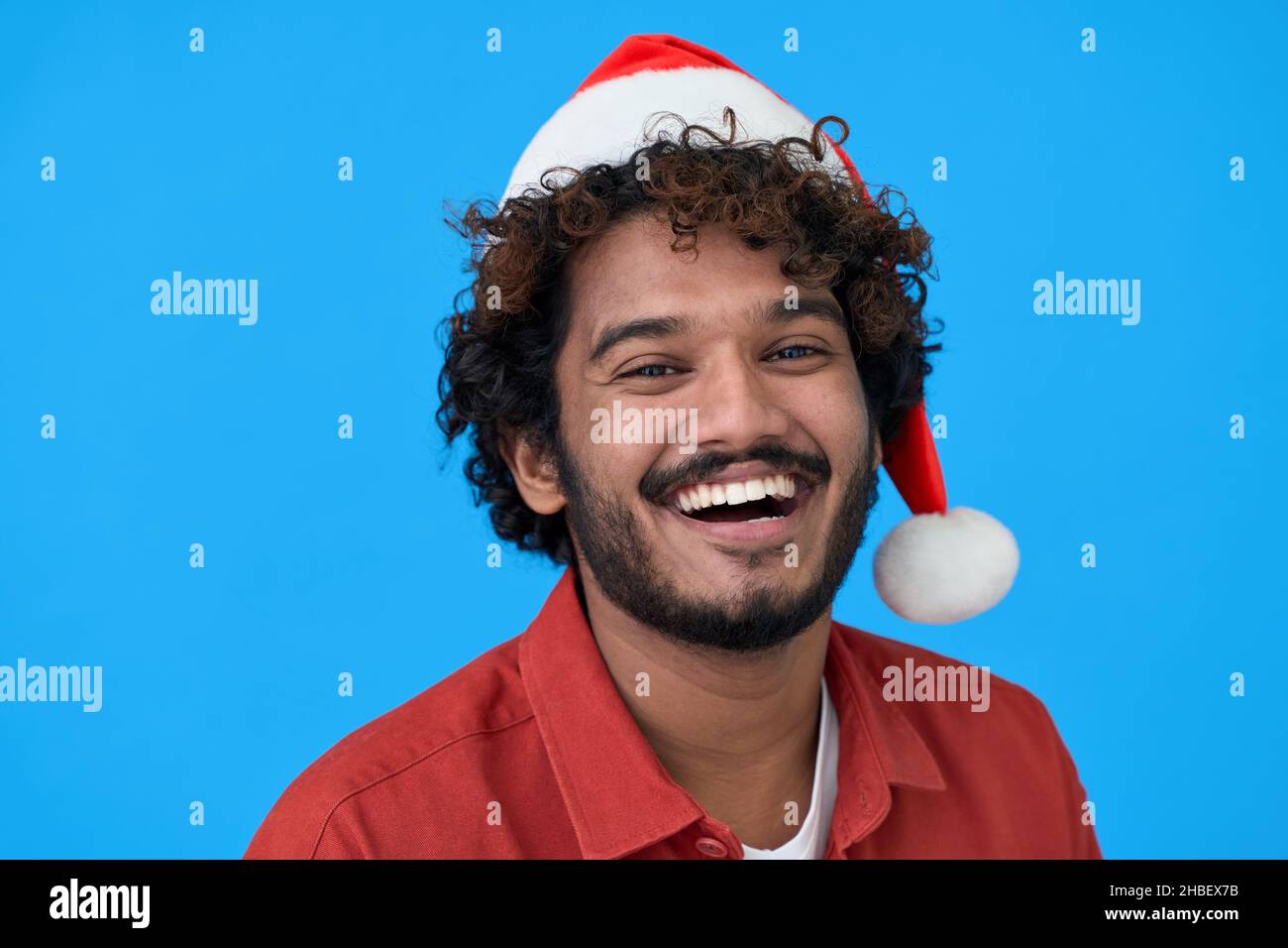 Glücklicher junger indischer Mann mit santa Hut isoliert auf blauem Hintergrund. Stockfoto