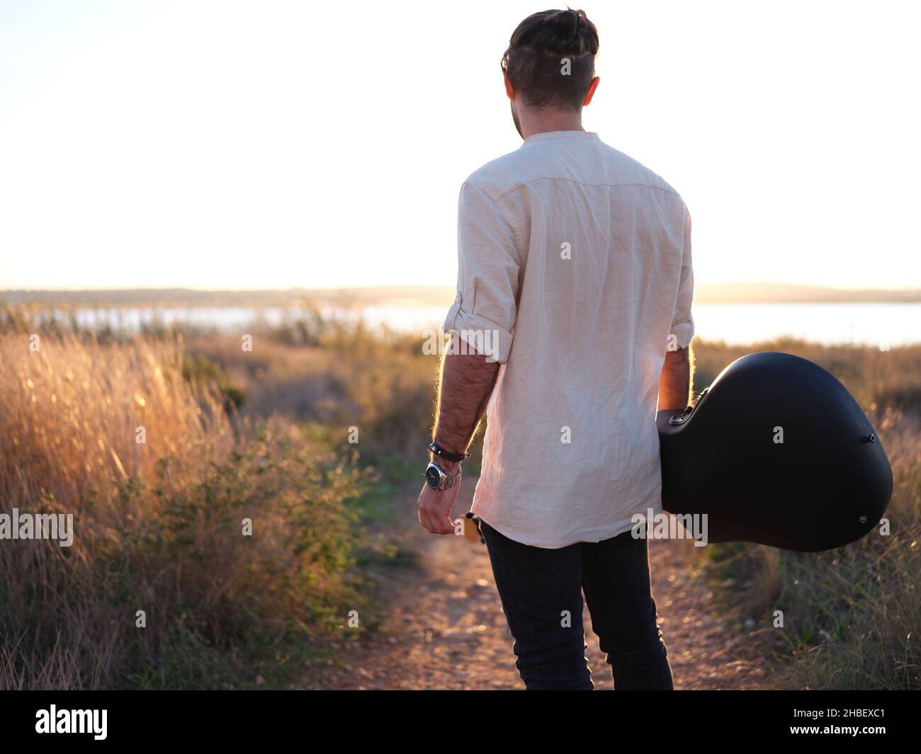 Musiker, der den Sonnenuntergang mit seiner Gitarre in der Hand betrachtet Stockfoto