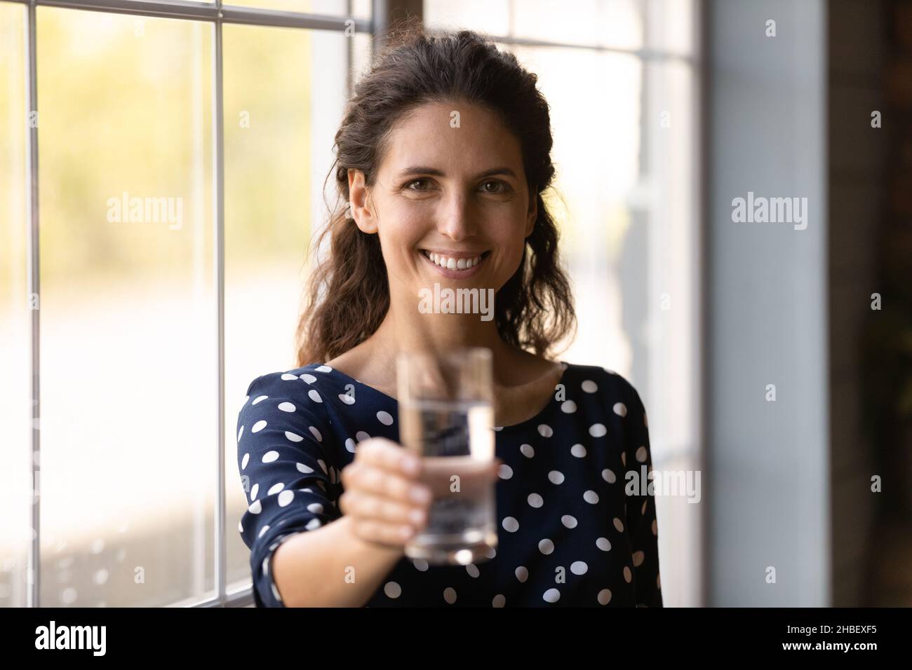 Porträt einer lächelnden lateinischen Frau mit einem Glas kühlem Mineralwasser, Stockfoto
