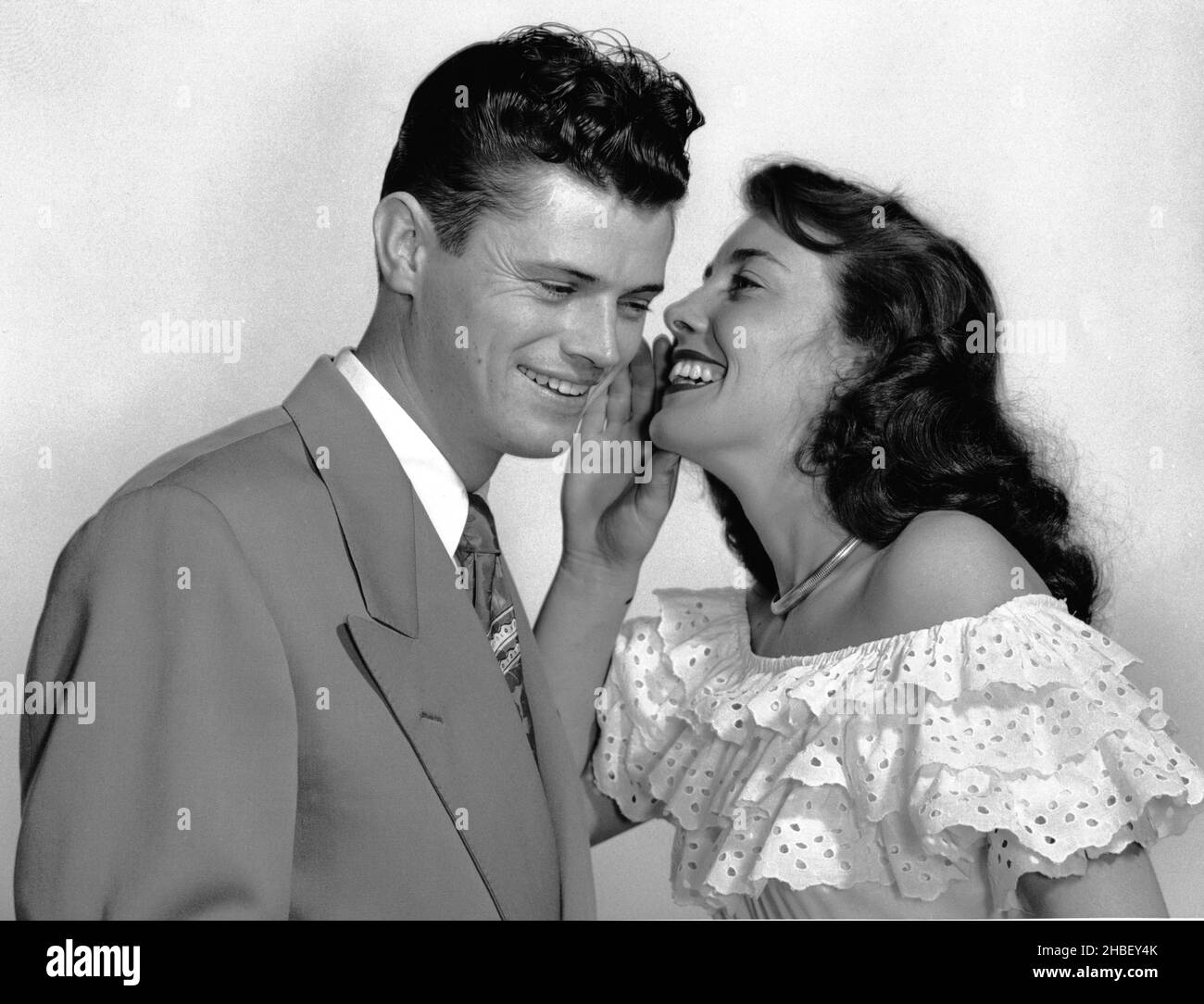 Junge Männer und Frauen in den 30er Jahren, gut gekleidet, posierten,  während Frau dem Mann ein Geheimnis flüstert. Beide lächelten. Ca. 1960  Stockfotografie - Alamy