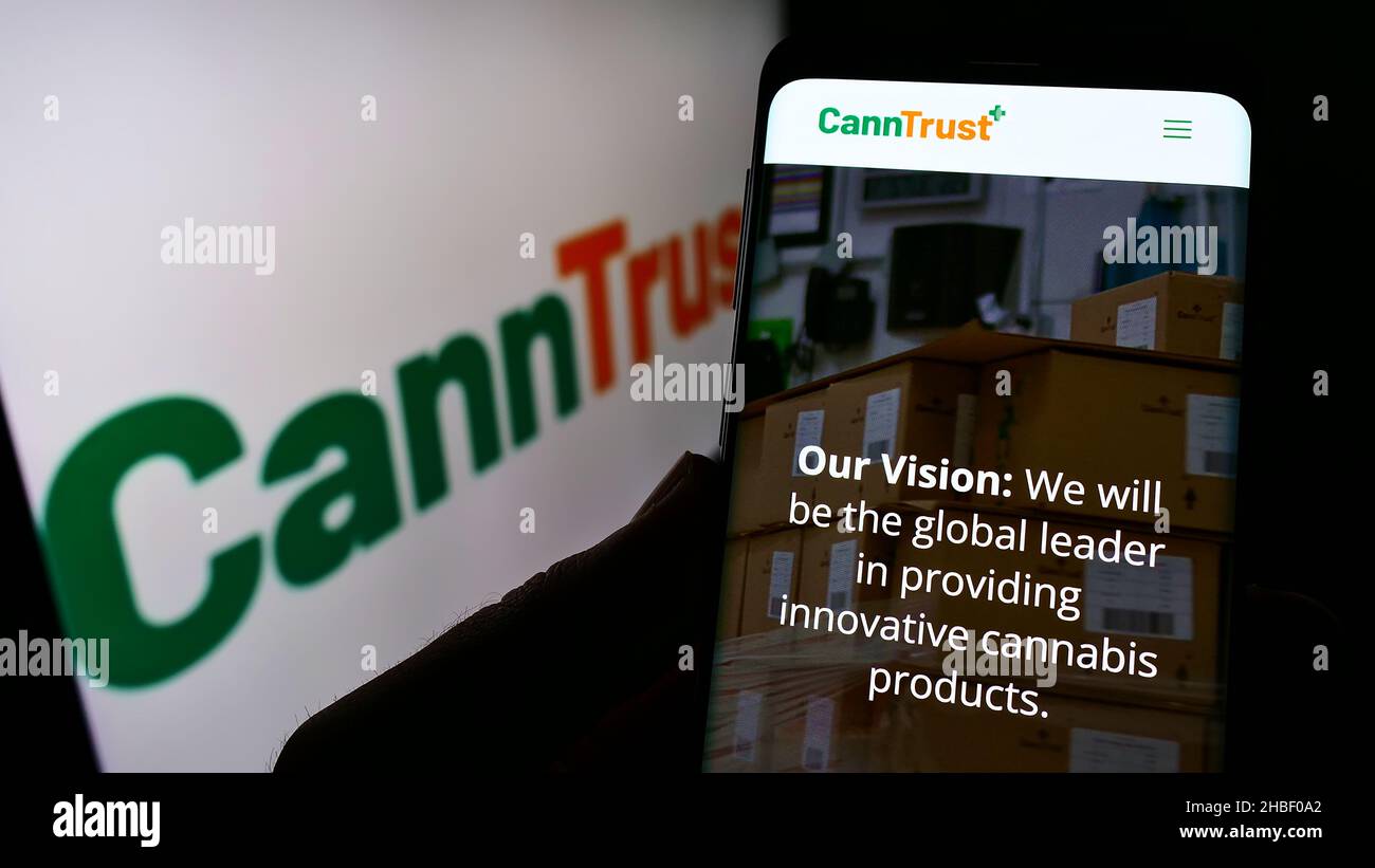 Person, die Mobiltelefon mit der Webseite des kanadischen Cannabisunternehmens CannTrust Holdings Inc. Auf dem Bildschirm mit Logo hält. Konzentrieren Sie sich auf die Mitte des Telefondisplays. Stockfoto