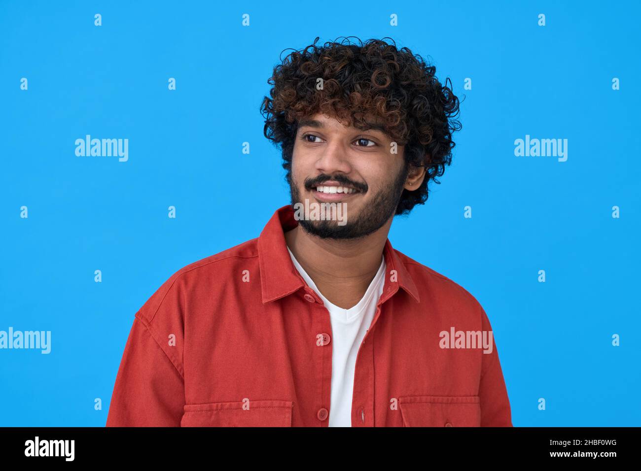 Glücklich lächelnder junger indischer Mann, der auf blauem Hintergrund träumt. Stockfoto