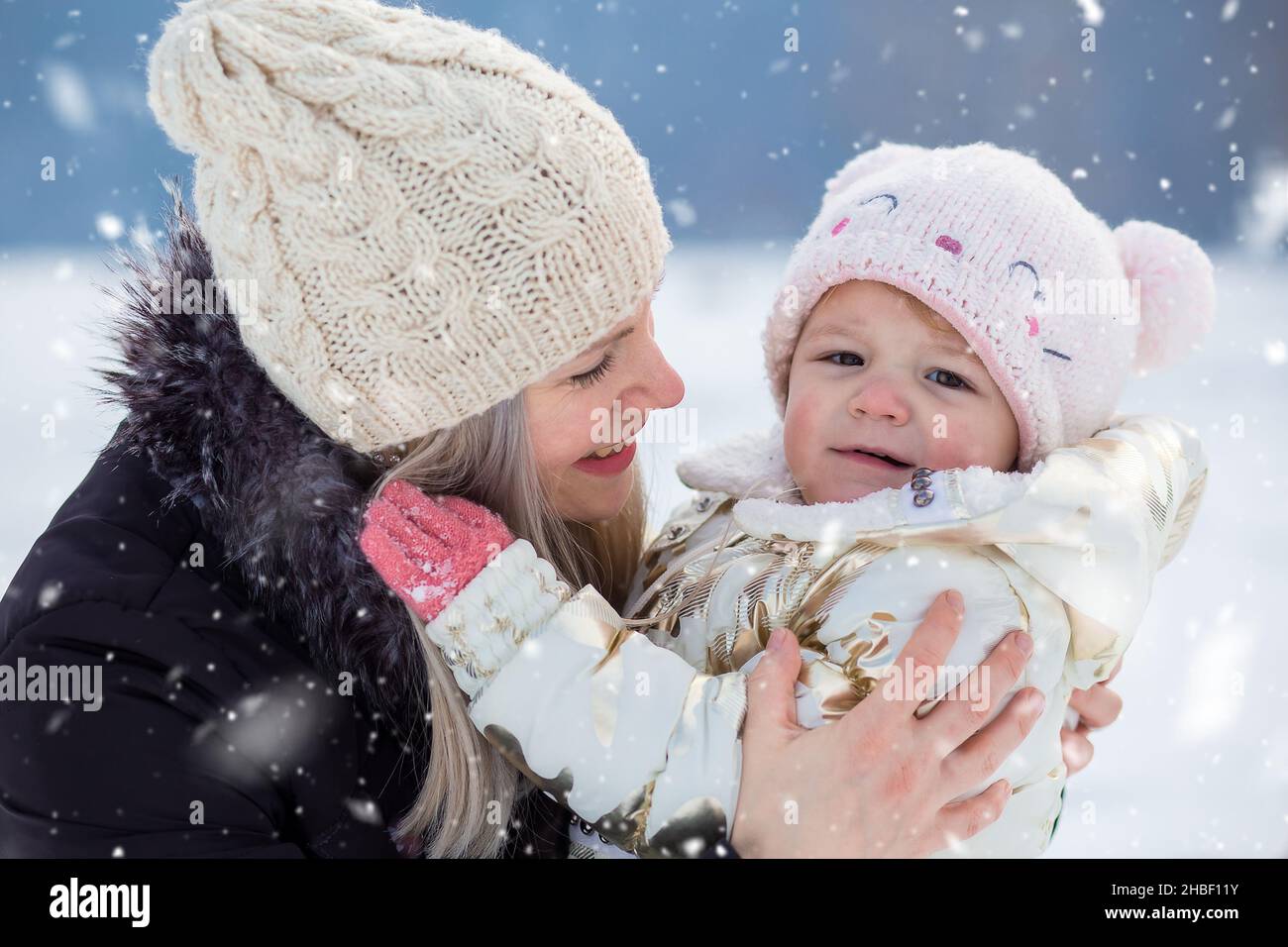 Die junge Mutter umarmt ihre kleine Tochter. Winterzeit, Outdoor-Aktivitäten Stockfoto