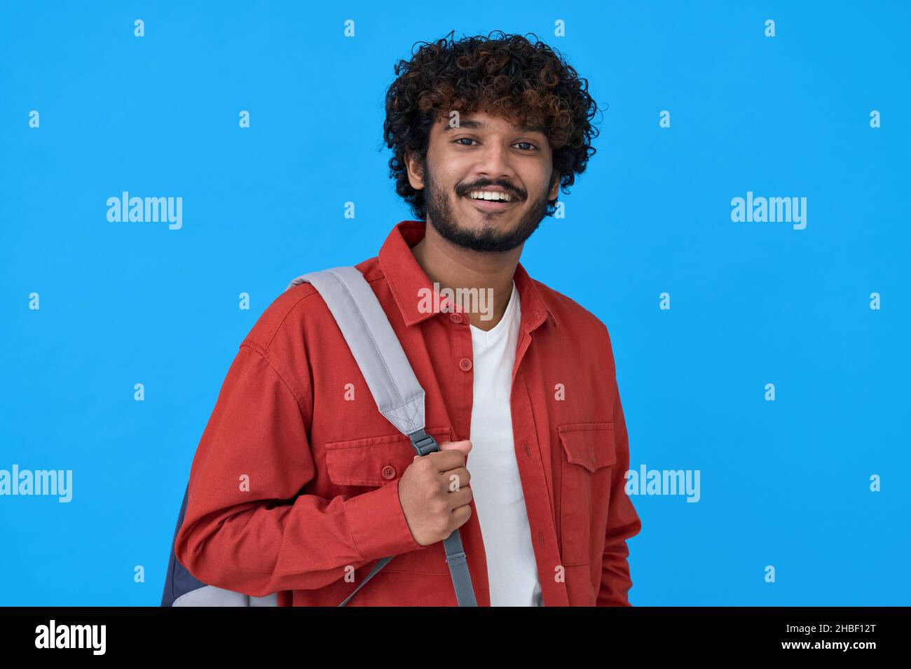 Glücklich junge indische Kerl hält Rucksack isoliert auf blauem Hintergrund. Stockfoto