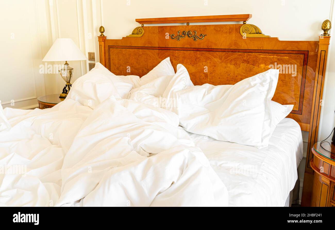 Ungeschmachtes Bett mit zerknitterter Bettwäsche, Bettwäsche und Laken in einem leeren, luxuriösen Hotelzimmer Stockfoto