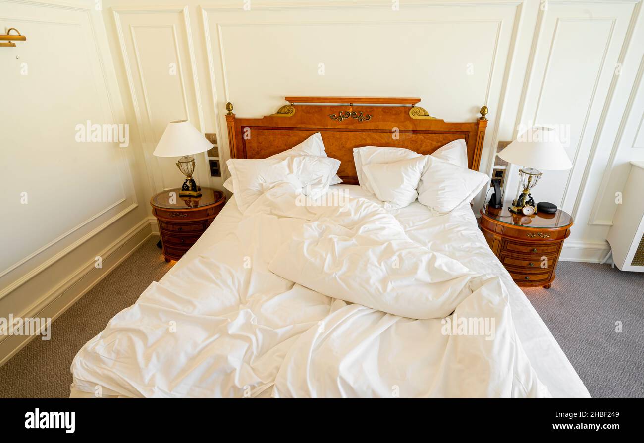 Ungeschmachtes Bett mit zerknitterter Bettwäsche, Bettwäsche und Laken in einem leeren, luxuriösen Hotelzimmer Stockfoto