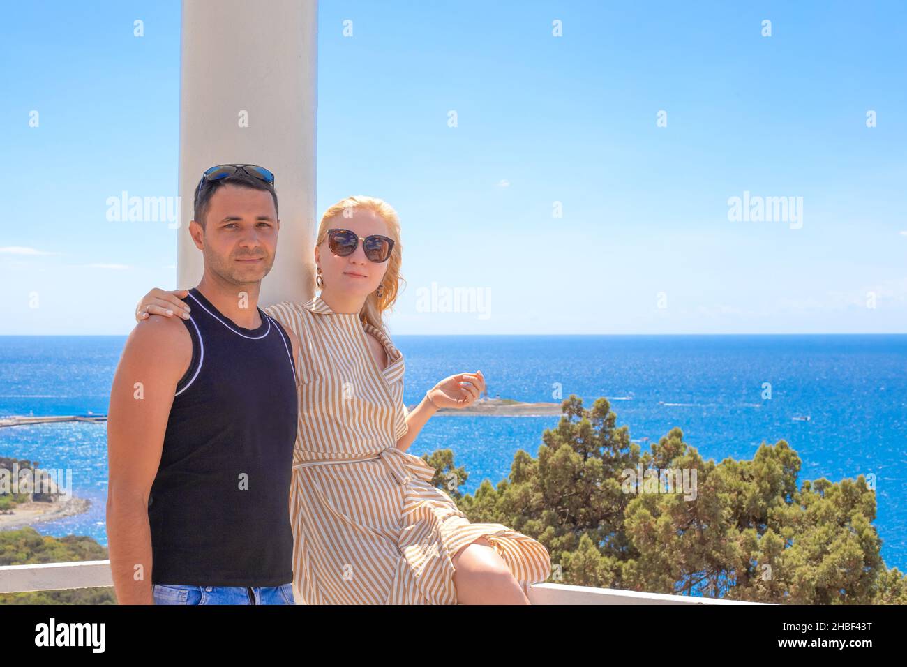 Junge Familie, eine Frau umarmt einen Mann in einem Pavillon mit Blick auf das blaue Meer. Reisen und Tourismus im Sommer. Speicherplatz kopieren. Stockfoto
